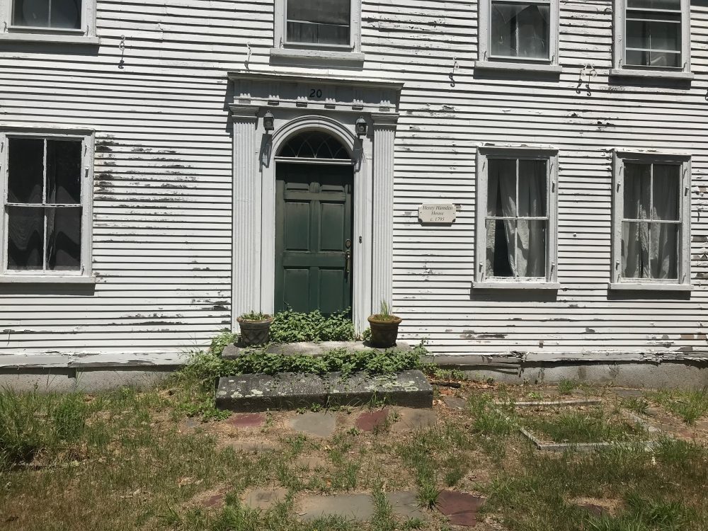 The house before rehabilitation, in peeling white clapboard with an overgrown front step